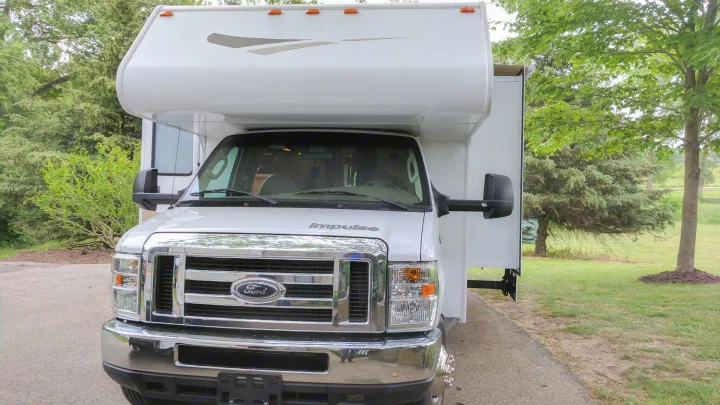 Front view of a white Ford Itasca Impulse Class C RV, parked among green trees. An ideal rv rental.. Winnebago ITASCA 2009