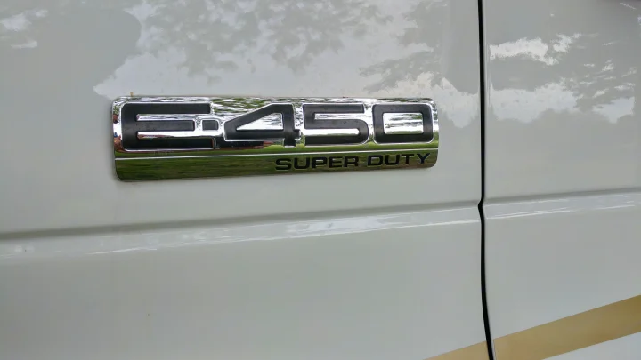 Close-up of an E-450 Super Duty badge on a white RV rental, showing the side panel with reflections.. Winnebago ITASCA 2009