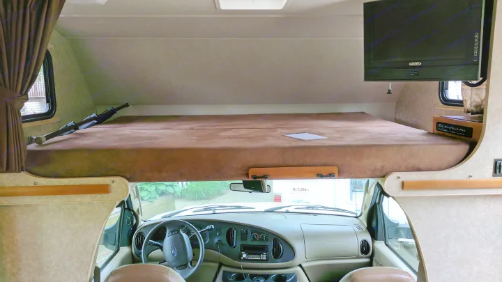 Cozy RV rental interior showcasing a spacious cab-over bunk, driver's dashboard, and front window view.. Winnebago ITASCA 2009