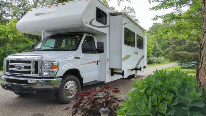 This modern white Class C Itasca Impulse RV rental is parked with its slide-out extended amidst green nature.. Winnebago ITASCA 2009