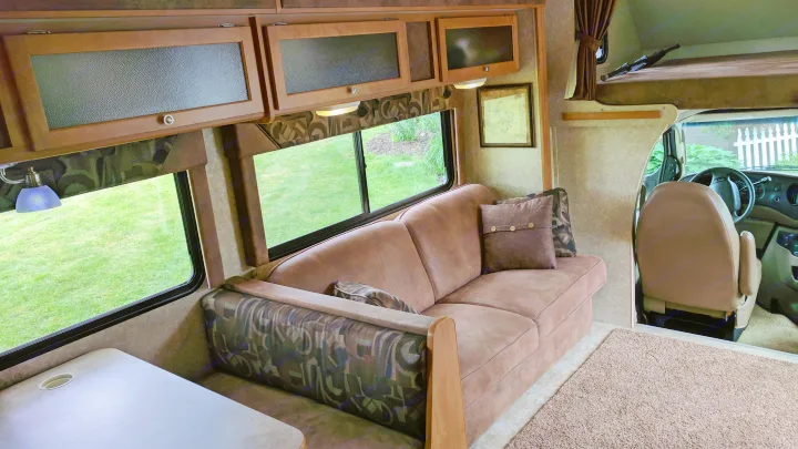 Inside a comfortable RV rental: Sofa, dinette, overhead cabinets, and large windows revealing a green lawn outside.. Winnebago ITASCA 2009