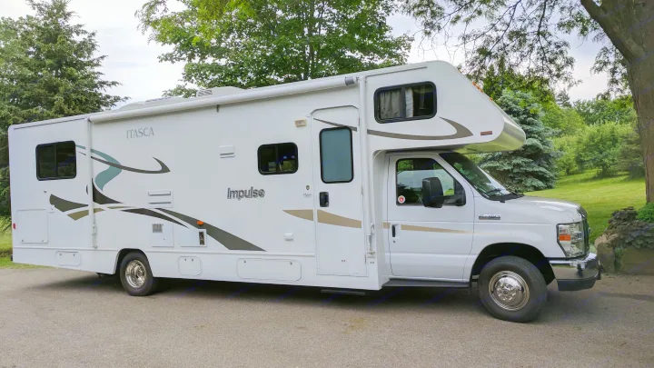White Itasca Impulse Class C RV rental, a motorhome with green trees and grass in the background, parked on pavement.. Winnebago ITASCA 2009