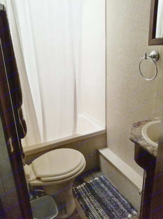 Compact RV rental bathroom: features a toilet, shower/tub, and sink vanity with mirror. White curtain and patterned rug.. Keystone Hideout 2017