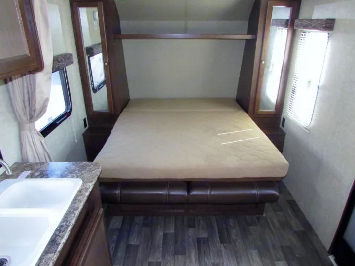 RV rental interior: A cozy convertible bed/sofa with side cabinets, a shelf above, and a kitchen sink on the left.. Keystone Hideout 2017