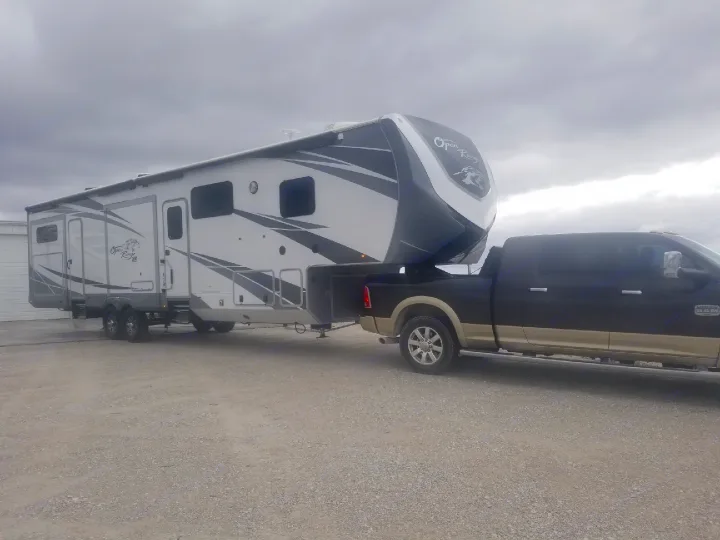 A large fifth-wheel RV, ideal for an RV rental, is hitched to a powerful pickup truck on a gravel lot under a cloudy sky.. Highland Ridge Open Range 427BHS 2019