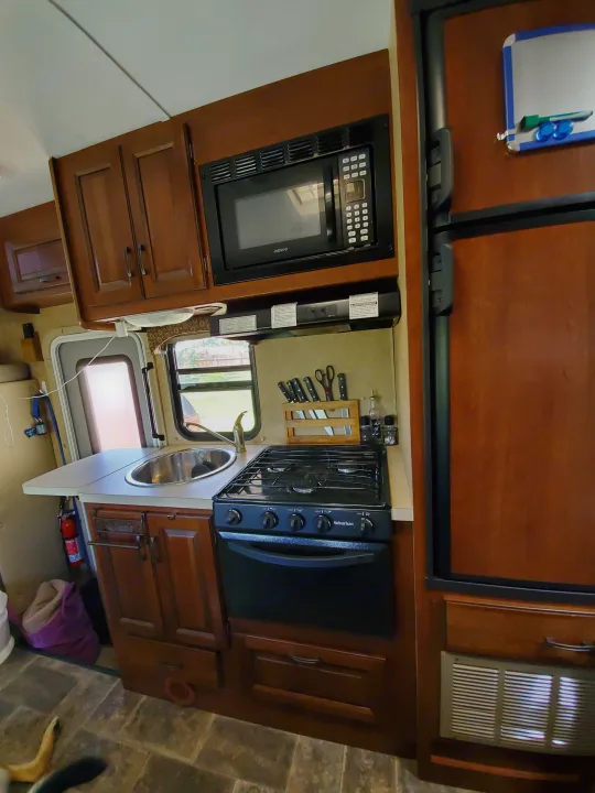 RV rental kitchen: dark wood cabinets, Advent microwave, Suburban stove, sink, and refrigerator. Essential for travel comfort.. Forest River Forester 2015