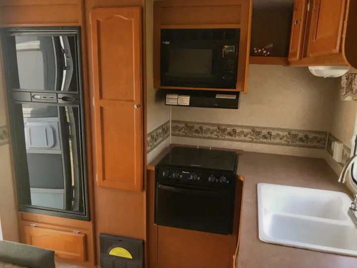 RV rental kitchen showcasing black appliances: a tall fridge, microwave, stove, and a white double sink.. Dutchmen Dutchmen 2007