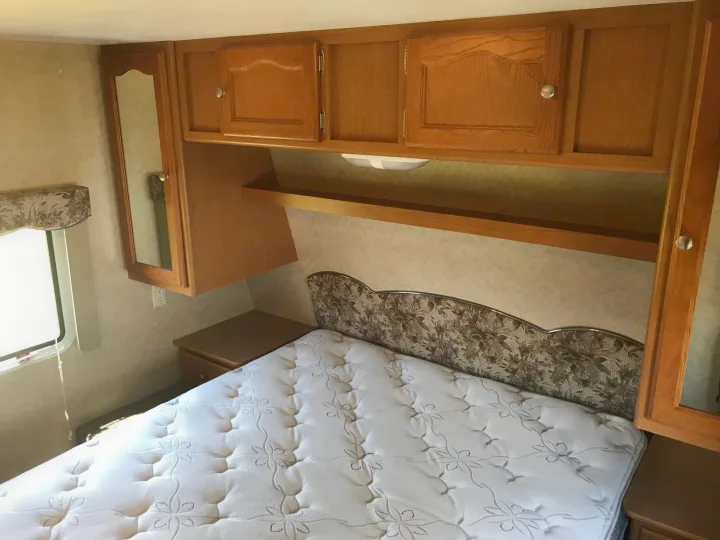Cozy RV rental bedroom featuring a bed with patterned mattress, floral headboard, and wood cabinetry.. Dutchmen Dutchmen 2007