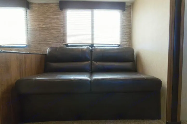 This RV rental features a dark brown faux leather sofa positioned under two bright windows, offering comfortable interior seating.. Gulf Stream Kingsport 2019