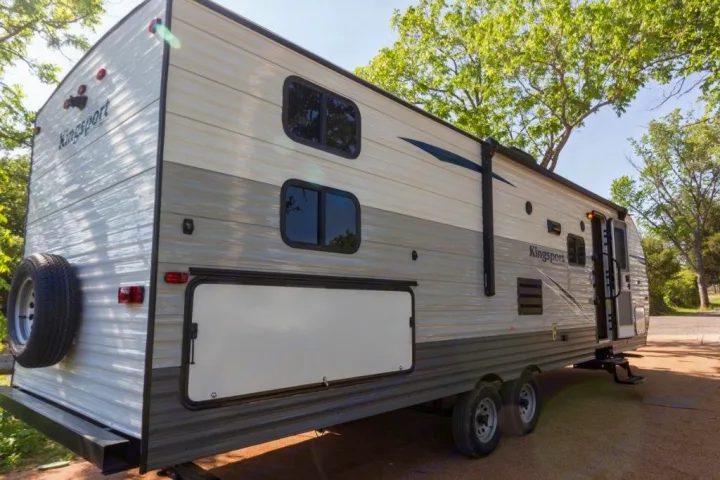A light-colored Kingsport travel trailer RV rental. Features: dual axles, side entry, windows, and a rear spare tire.. Gulf Stream Kingsport 2019