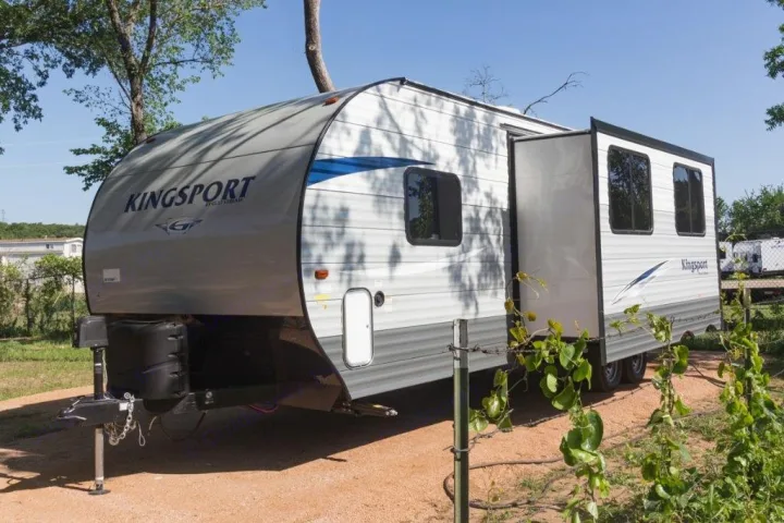 A gray and white Kingsport travel trailer RV rental with an extended slide-out, parked at a sunny campsite.. Gulf Stream Kingsport 2019