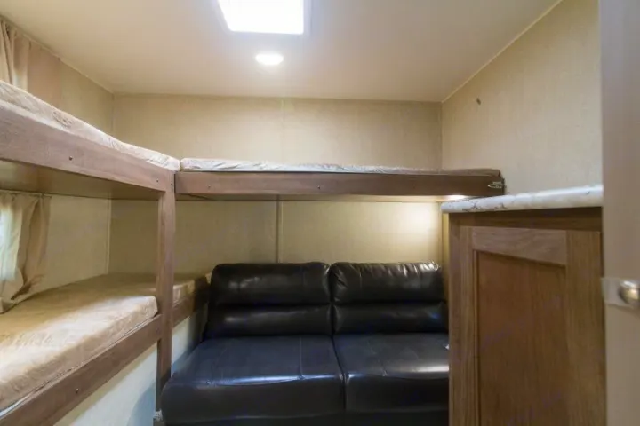 Spacious RV rental bunkhouse interior with comfortable black sofa & multiple wooden bunk beds, illuminated by a skylight.. Gulf Stream Kingsport 2019