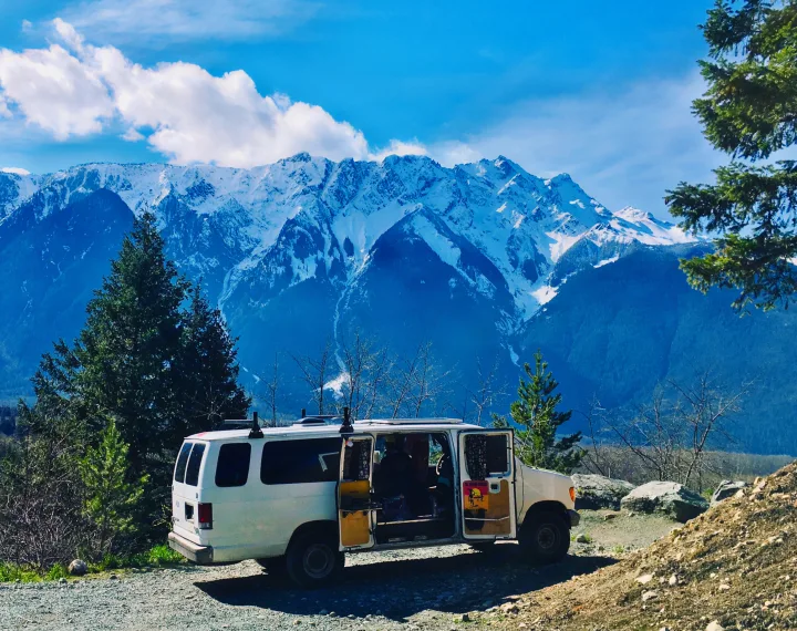 White RV rental van parked on a gravel road, facing majestic snow-capped mountains & blue skies. Ideal for nature adventures.. Ford Ford E350 1996
