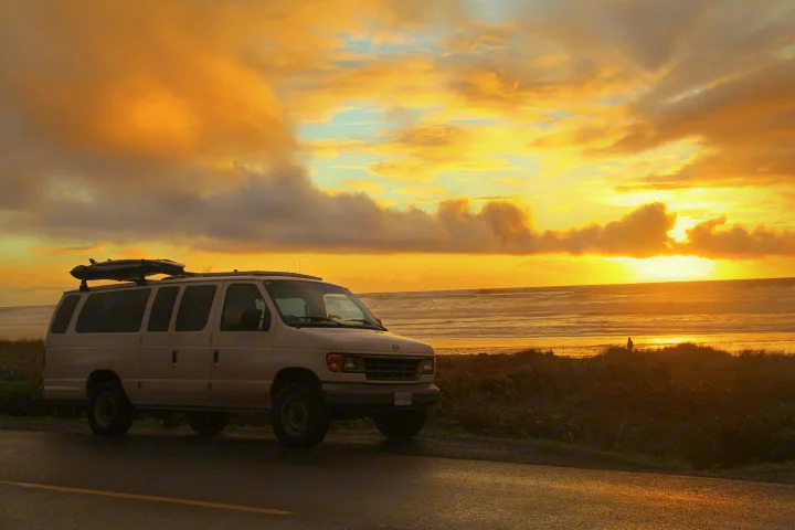 Gorgeous sunset illuminates a white van by the beach. Waves crash as a person enjoys the view. Consider this RV rental for your next road trip.. Ford Ford E350 1996