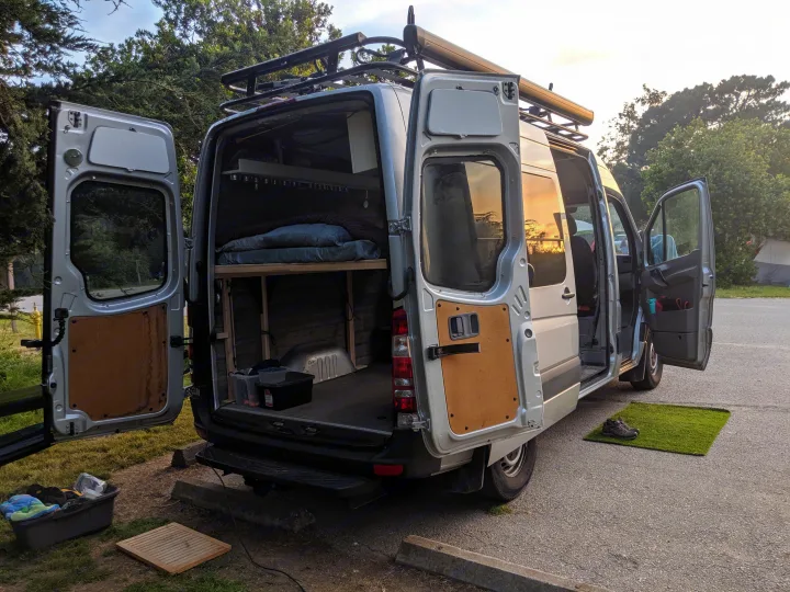Open doors showcase this RV rental's custom Sprinter van conversion & comfy camp setup at sunset.. Mercedes-Benz Sprinter 2016