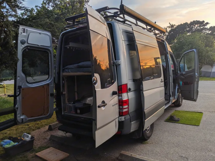 A detailed view of an RV rental Sprinter camper van at dusk, with all doors open, showing its ready-to-camp setup.. Mercedes-Benz Sprinter 2016