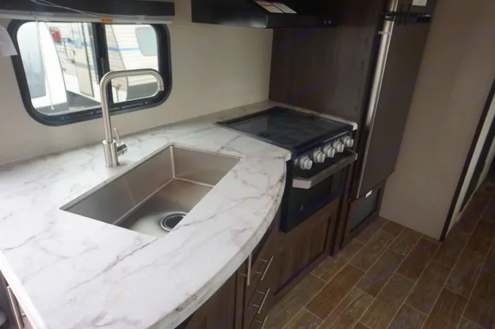 Inside an RV rental: a clean, modern kitchen with white marble-look counters, stainless steel sink, stove, and fridge.. K-Z Manufacturing sportsmen 301 2020