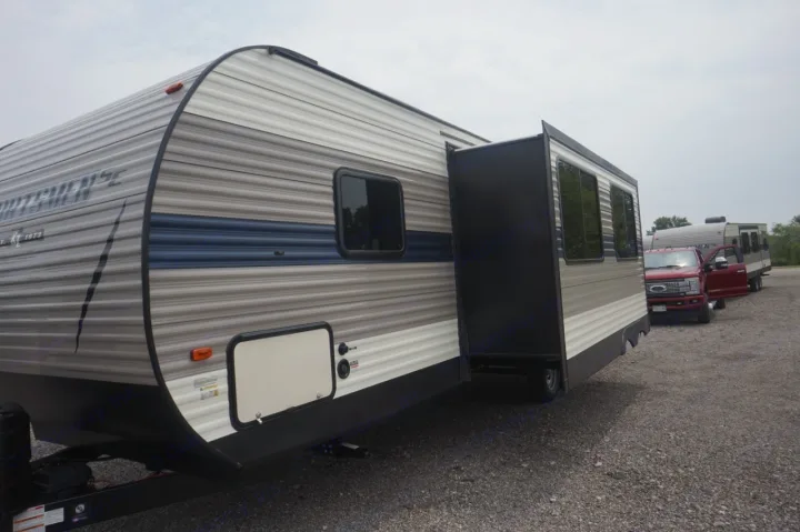 RV rental: Travel trailer with slide-out extended, gray and blue, parked on a gravel lot. Red truck nearby.. K-Z Manufacturing sportsmen 301 2020