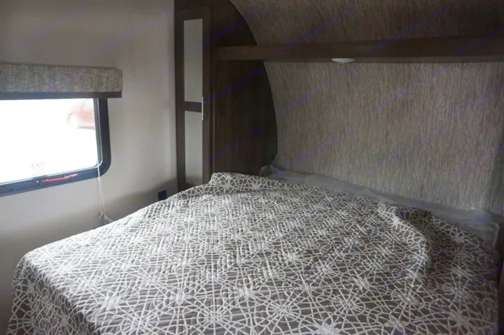 Comfortable RV rental bedroom with a patterned quilt, window with an EXIT sign, and built-in storage.. K-Z Manufacturing sportsmen 301bhse 2020