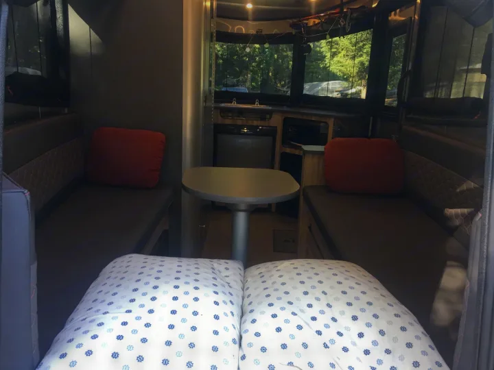 RV rental interior: Cozy dining/sleeping area with a kitchen, large windows, and a view of trees outside.. Airstream Base Camp 2017