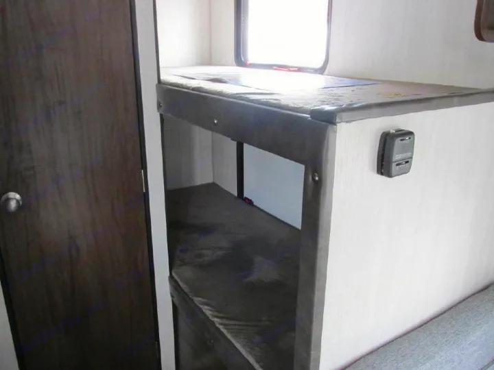 Inside an RV rental: view of a compact sleeping area with upper and lower bunk beds, adjacent to a wooden door.. Forest River Cherokee Wolf Pup 2019
