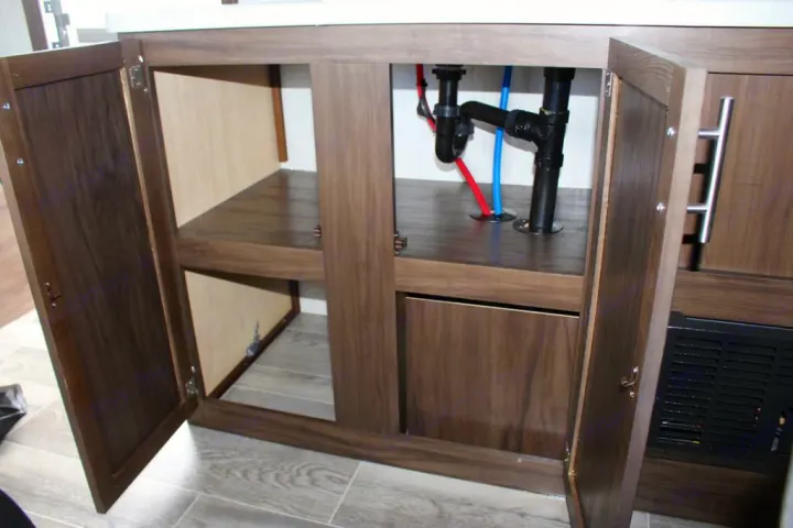 RV rental: Open under-sink cabinet in RV, revealing plumbing & storage shelves.. Forest River Cherokee Wolf Pup 2019