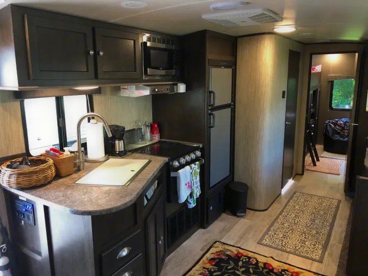 RV rental kitchen: features a sink, microwave, stove, fridge, and a hallway leading to a bunk area.. Heartland Sundance 2019