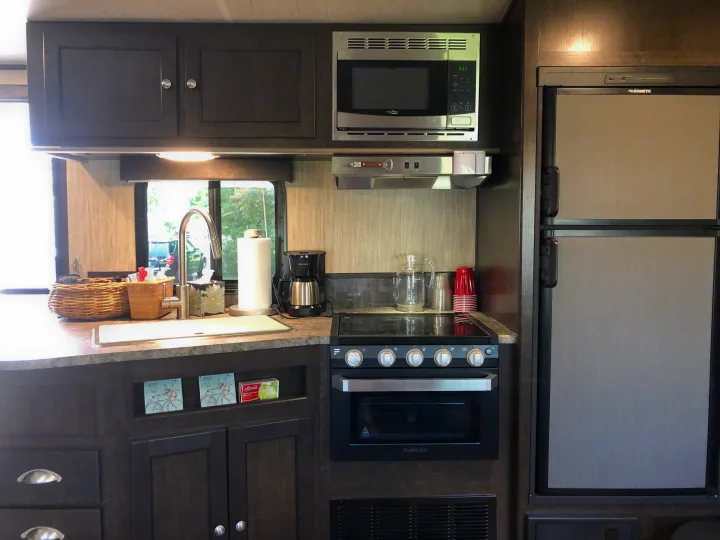 This well-equipped RV rental kitchen features a Dometic refrigerator, Furrion oven, microwave, sink, and various kitchen essentials.. Heartland Sundance 2019