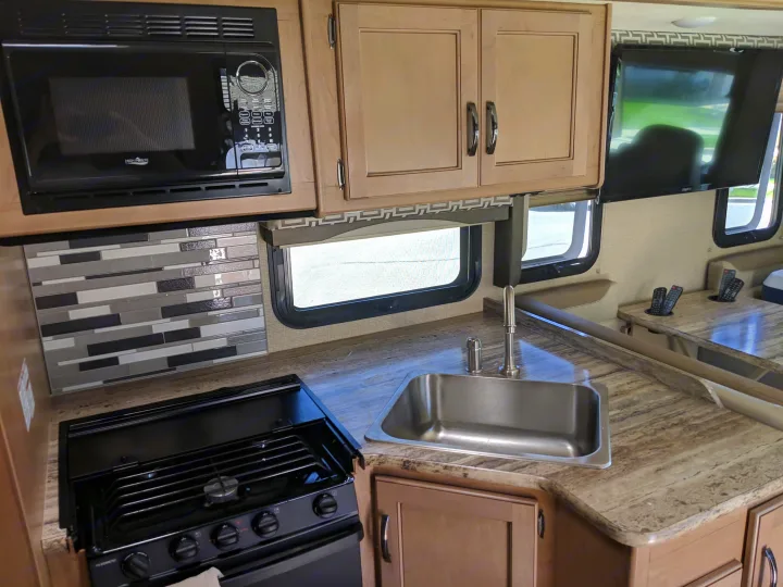 RV rental's modern kitchen boasts a microwave, stove, sink, tiled backsplash, and light wood cabinets.. Thor Motor Coach A.C.E 2019