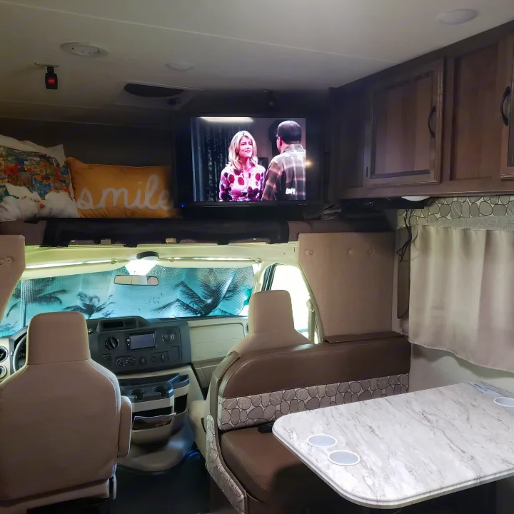 Inside an RV rental: a cozy dinette with patterned cushions, a mounted TV, and the front cockpit area with a sunshade.. Coachmen Freelander BH31 2019