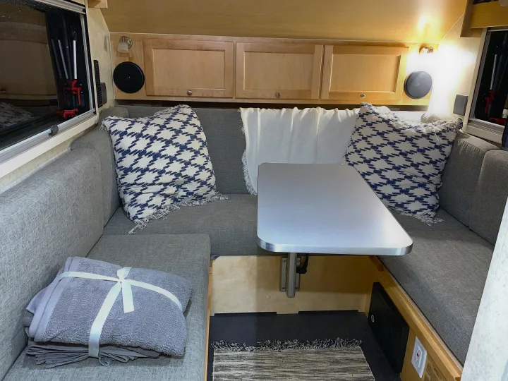 Step into this cozy RV rental's interior, featuring grey dinette seating, a central table, and overhead cabinets.. T@B Other 2019