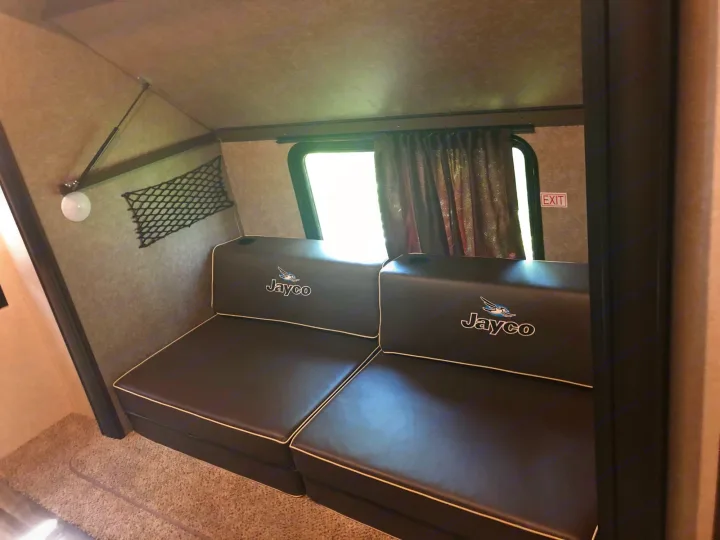 RV rental interior with dark Jayco seating, side window, EXIT sign, and wall storage. A cozy space for your travels.. Jayco Other 2020