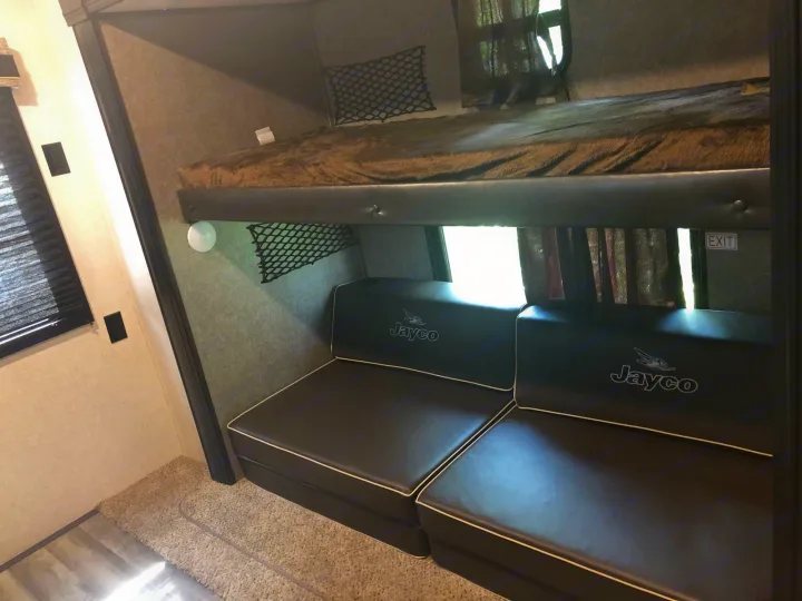 Inside an RV rental: view of bunk bed with cozy blanket, lower Jayco branded seating, and storage nets. Compact, functional space.. Jayco Other 2020