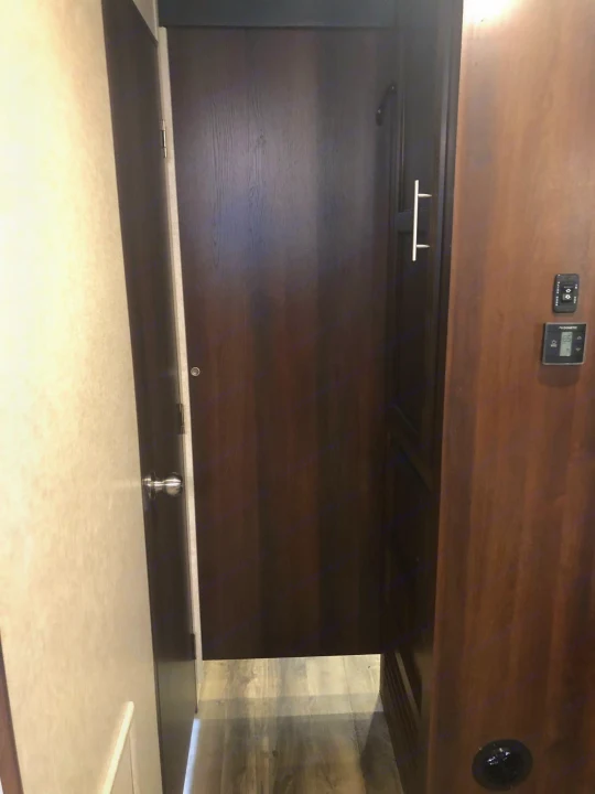 Inside an RV rental: a dark wood door with a silver pull handle dominates a narrow passage. A Dometic thermostat is on the right wall.. Jayco Other 2020