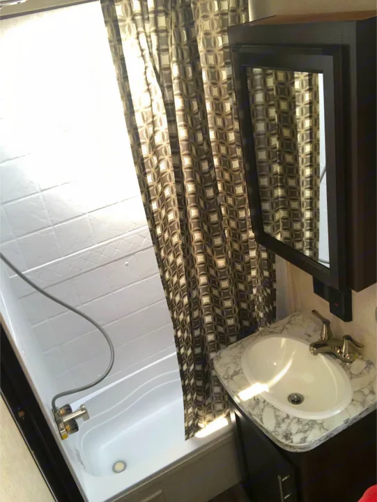 Compact RV rental bathroom features a white shower/tub, patterned curtain, and vanity with sink & mirror, ideal for travel.. Jayco Other 2020