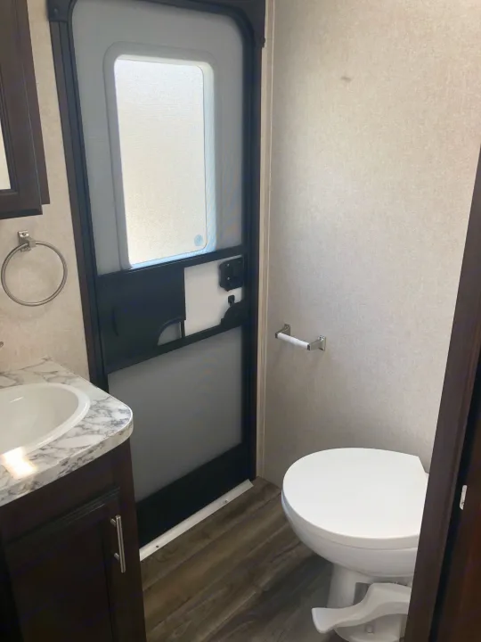 Inside an RV rental, this clean, compact bathroom features a sink, toilet, and the main entry door.. Jayco Other 2020