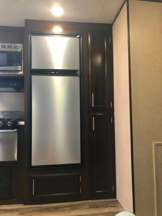 Inside an RV rental, showing a compact kitchen with stainless steel fridge, microwave, stove, & dark wood pantry.. Jayco Other 2020