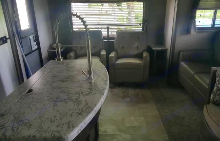 Spacious RV rental interior featuring a modern kitchen island with two faucets, recliners, and a comfortable sofa.. Forest River Surveyor 2018