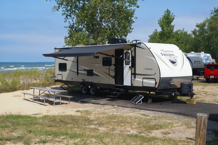 RV rental parked on a sandy beachfront site with an extended awning, a picnic table, and a portable solar panel.. Coachmen Freedom Express 2018