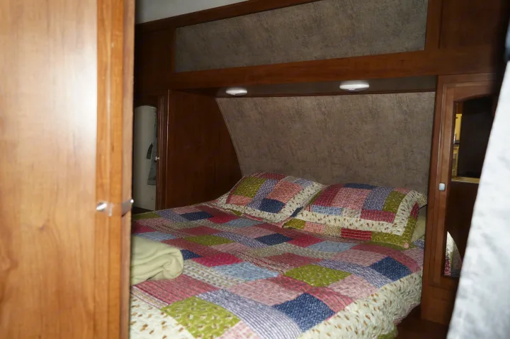 Cozy RV rental bedroom with a colorful patchwork quilt, overhead cabinets, and reading lights. Features wood accents and textured walls.. Coachmen Freedom Express 2017