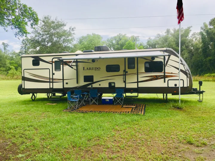 This Laredo RV rental travel trailer is set up with an awning, chairs, and cooler at a grassy campsite with a flag.. Keystone Laredo 2014