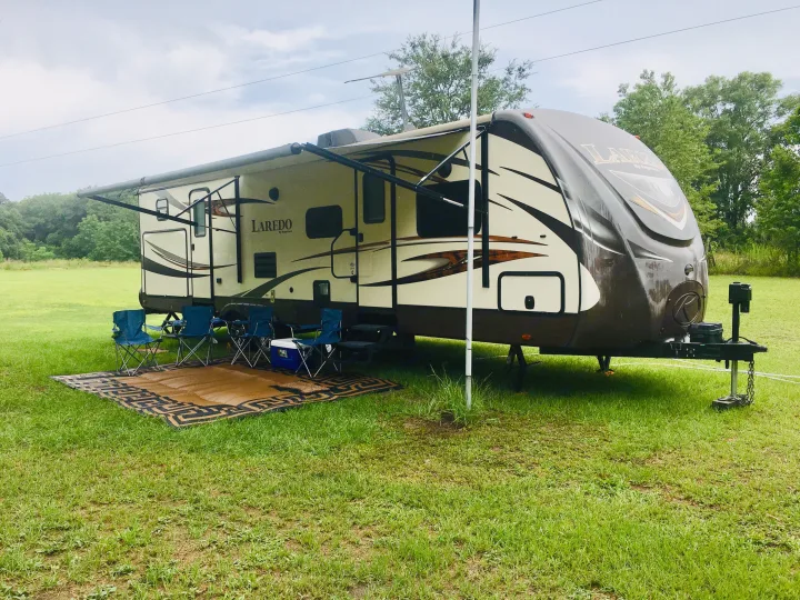 An RV rental, a Laredo travel trailer, is parked on green grass with its awning extended, blue chairs, and cooler set up.. Keystone Laredo 2014