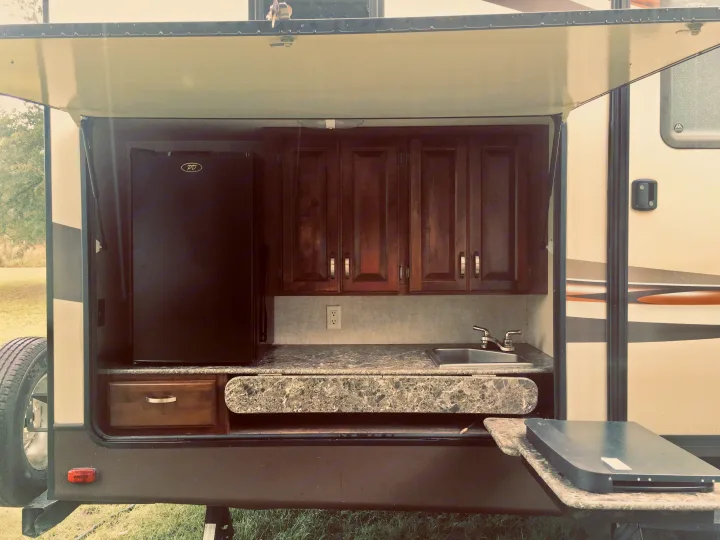 RV rental outdoor kitchen featuring a mini-fridge, sink, cabinets, and pull-out counter for convenient camping meals.. Keystone Laredo 2014