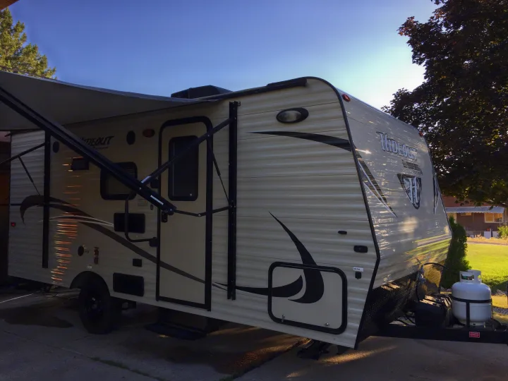 Light-colored travel trailer with extended awning & propane tank, ready for an RV rental.. Keystone Hideout 2016