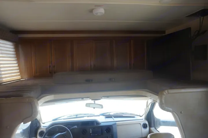 RV rental interior view: front cab, cozy overhead bunk bed with cushions, ample storage cabinets, and a mounted TV.. Gulf Stream conquest 2020