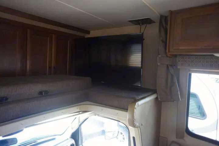View inside an RV rental of the cab-over bunk, a large TV, wood cabinets, and window.. Gulf Stream conquest 2020