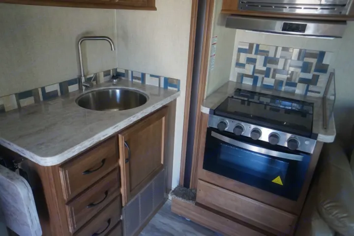 Compact RV rental kitchen with a stainless steel sink, pull-out faucet, gas stove, oven, and stylish patterned backsplash.. Gulf Stream conquest 2020