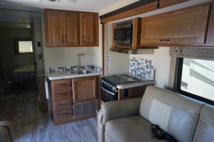 Inside an RV rental: a modern kitchen with microwave and stove, a comfy living area with a couch, and a peek into the bedroom.. Gulf Stream conquest 2020