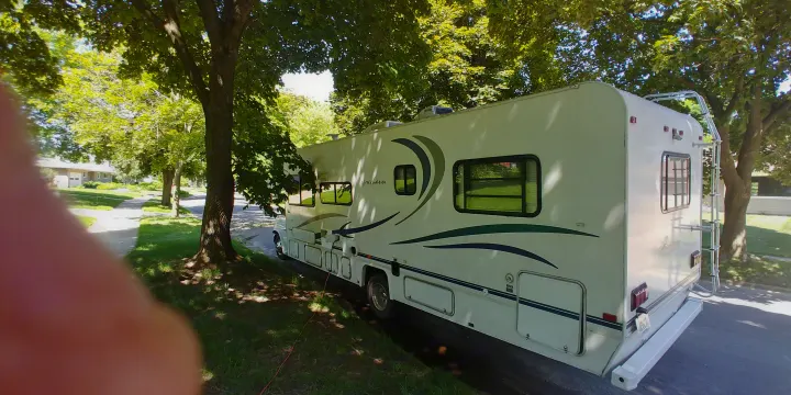 A white rv rental is parked under lush green trees on a sunny day, connected by a visible power cord, ready for your next adventure.. Coachmen Leprechaun 2001