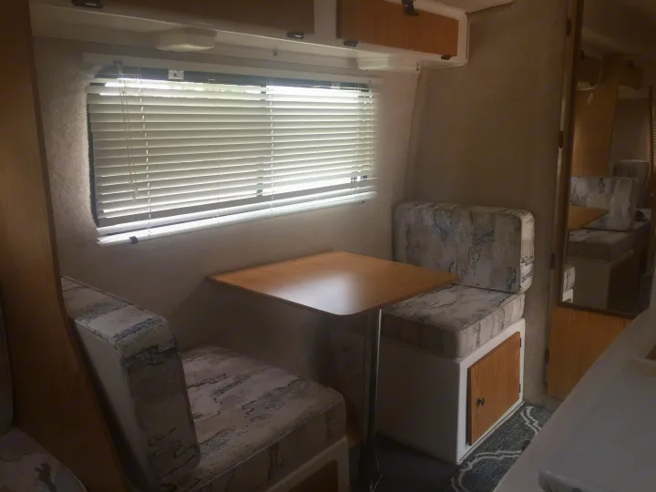 Cozy RV rental dinette setup with patterned benches, wooden table, and window blinds, perfect for travel accommodations.. Casita 17' Spirit Deluxe 2003